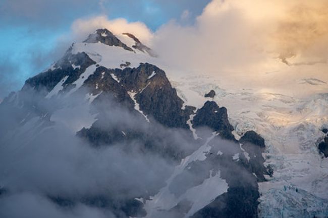 A majestic snow-capped mountain surrounded by clouds, creating a breathtaking and serene landscape.