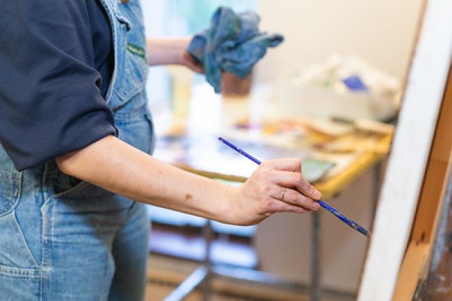A woman in overalls passionately painting on a canvas, expressing her creativity through vibrant strokes.