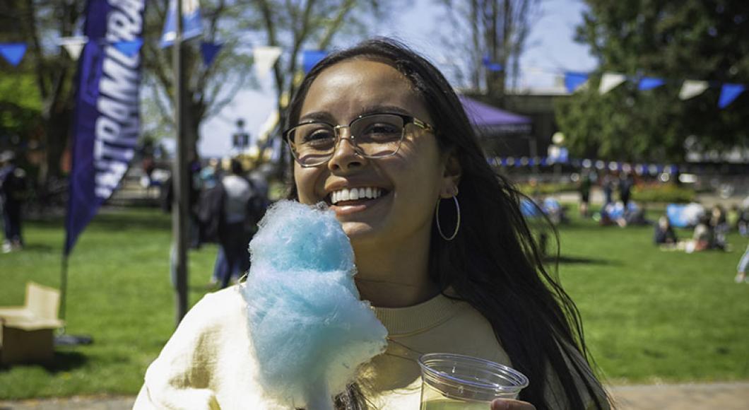 Smiling student holds cotton candy in her hand as she stands in a festive open space..